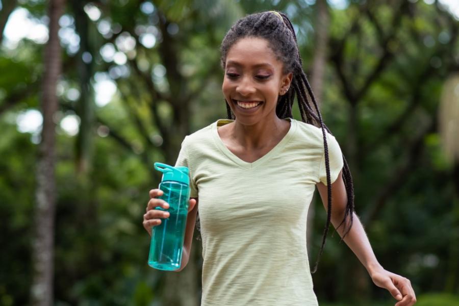 A smiling woman jogs while holding a water bottle