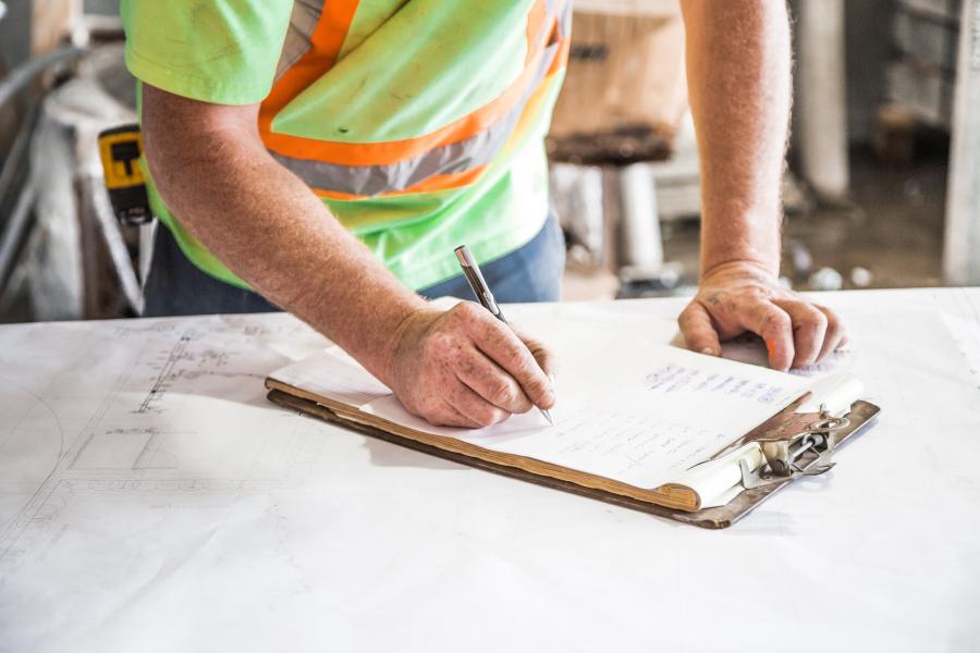 A man in a safety vest filling out paperwork on a clipboard