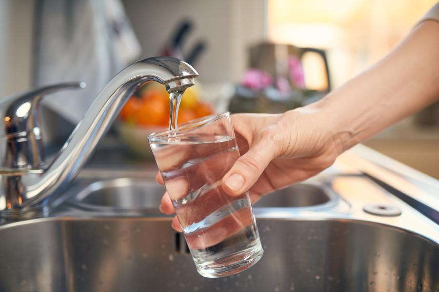 A hand holds a glass and fills it with water at a kitchen sink