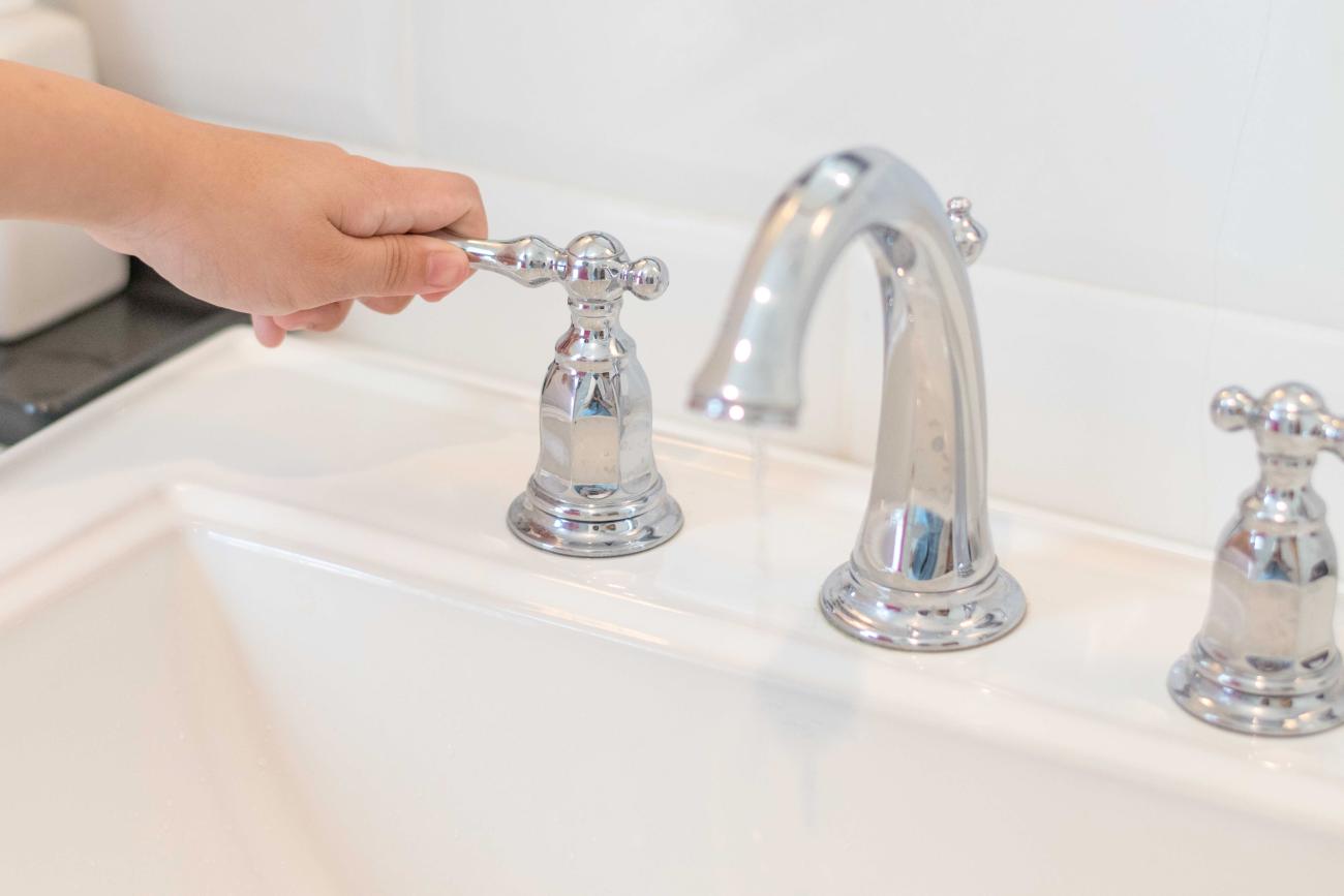 A hand turns off the handle on a faucet