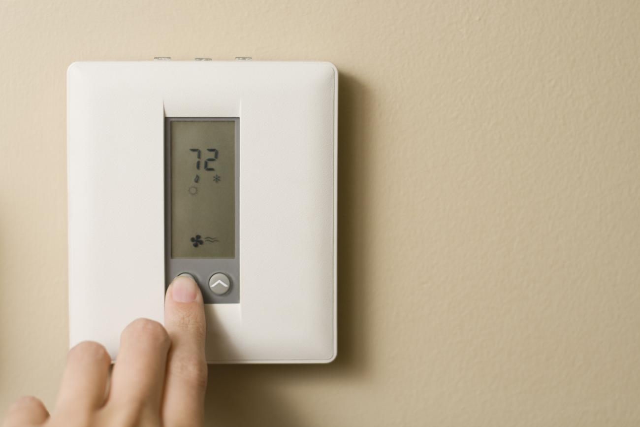 A woman's hand presses a button on a digital thermostat