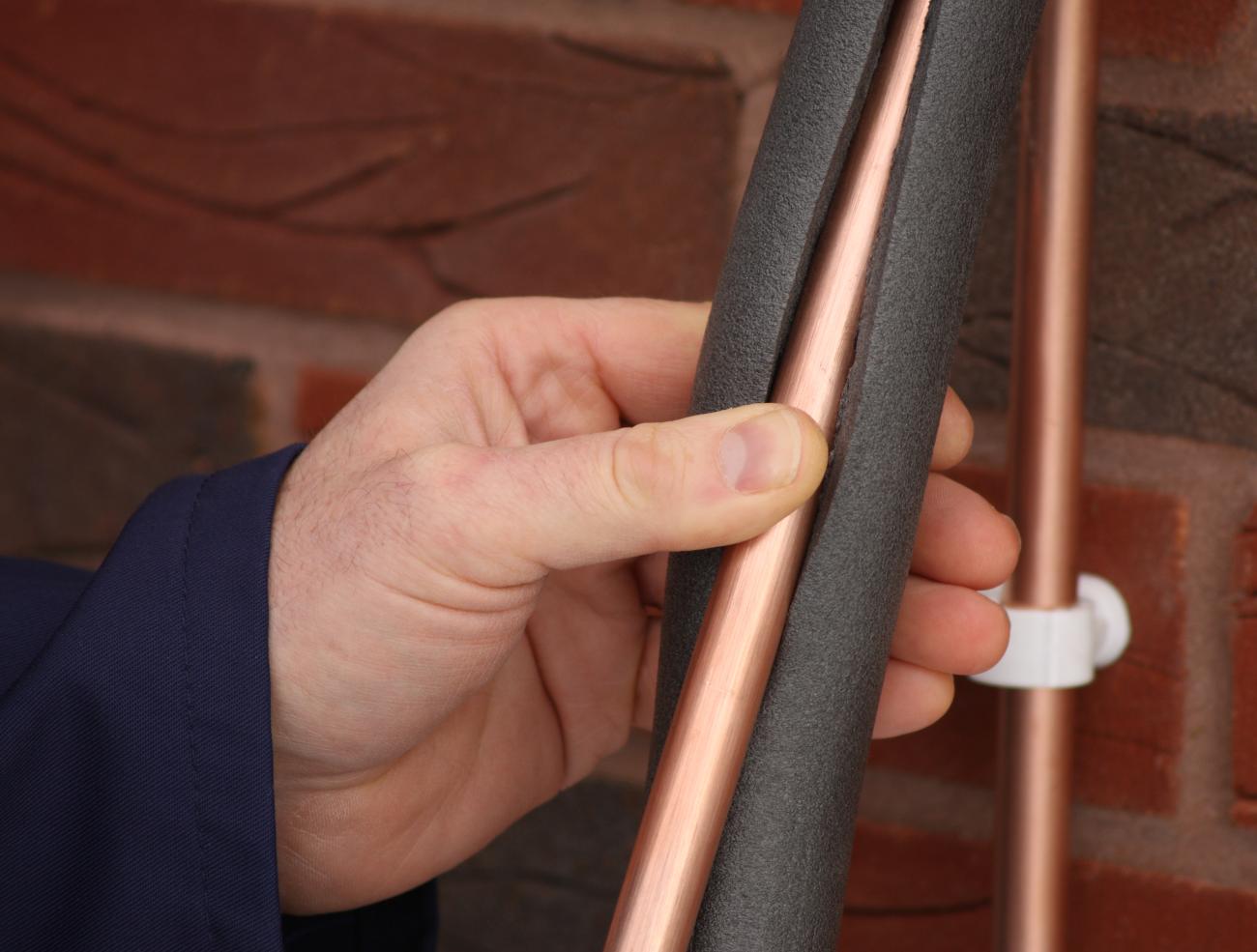 A man places foam insulation around a copper pipe