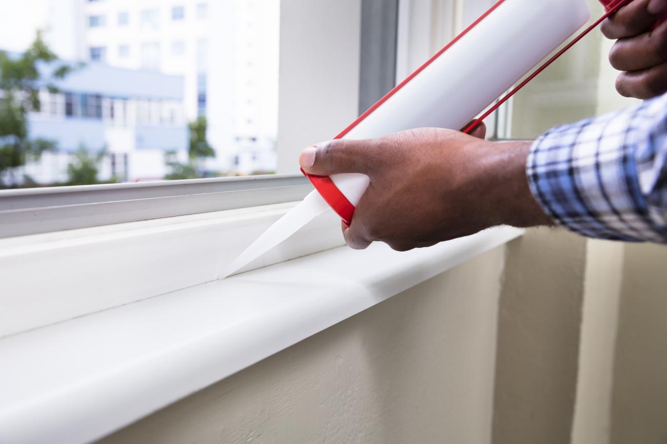 A man runs a bead of caulk along the inside of a window