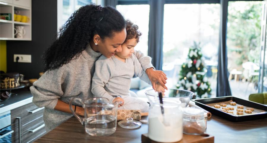 A mom and her young son are baking in the kitchen. Behind them is a Christmas tree.