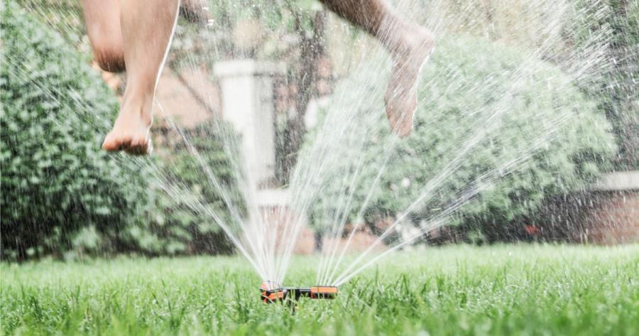 Two kids jump through a lawn sprinkler on a hot summer day