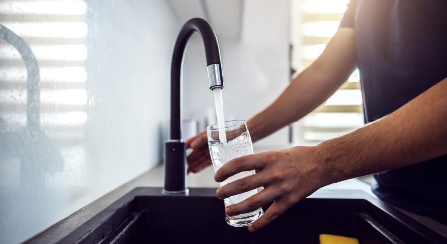 A man hold a glass and fills it with water at the kitchen sink