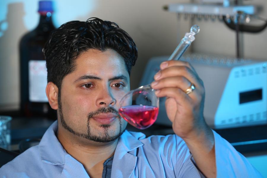 A man in a lab coat examines a glass beaker containing a pink liquid