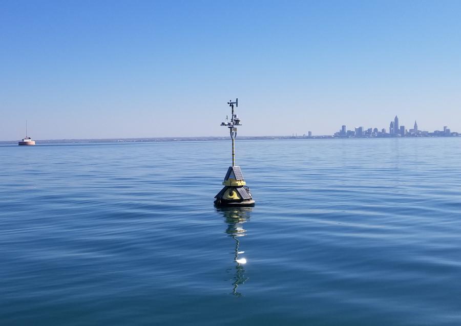 A yellow buoy floats in Lake Erie with the downtown Cleveland skyline in the distance