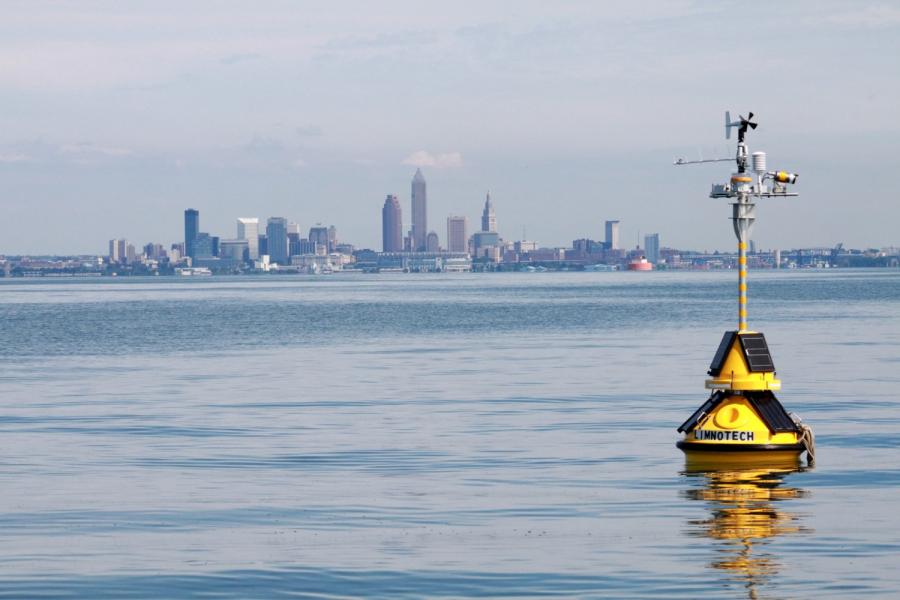 A yellow buoy floats in Lake Erie with the downtown Cleveland skyline in the distance