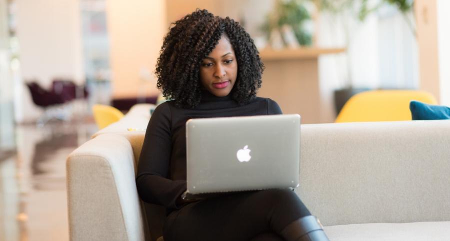 A woman sits on a couch looking at a laptop on her lap