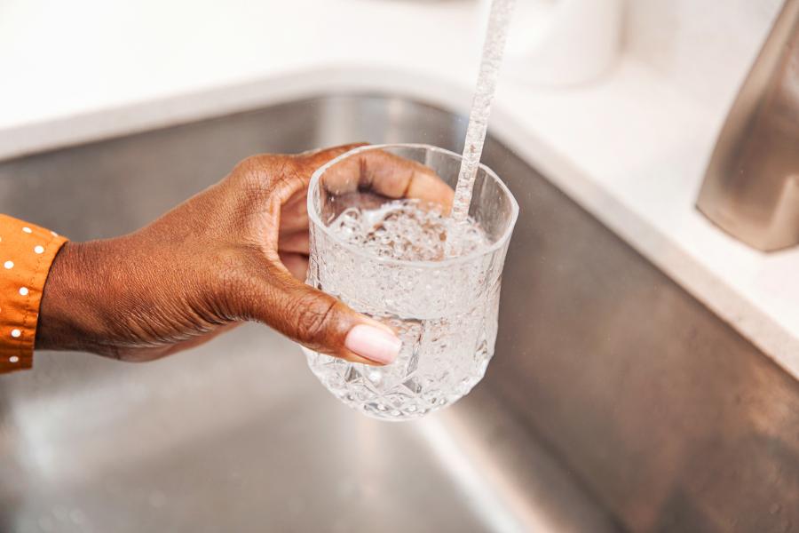 A woman fills a glass with water at a kitchen faucet