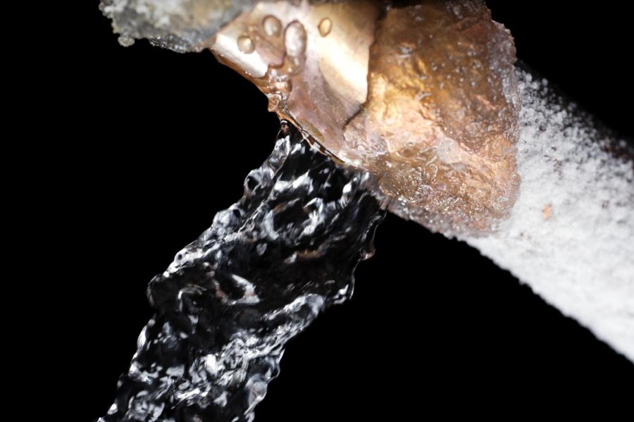 A close up of a copper pipe covered in frost and leaking water