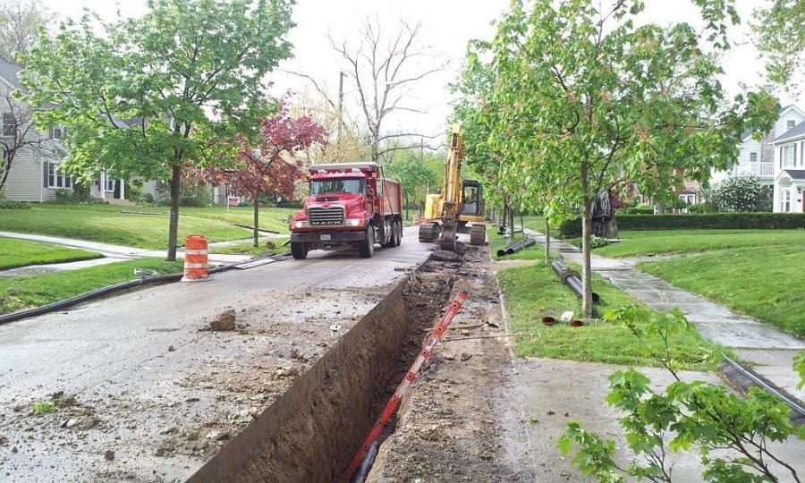 A residential street with a trench surrounded by construction crews and equipment 